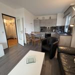 Wohnung mit Küche, Essbereich und Wohnzimmer. Schwarze Ledermöbel und Holzboden.