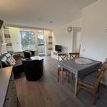 Wohn- und Essbereich mit Sofa, Tisch und Stühlen. Fenster mit Blick auf Balkon.