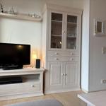 TV-Möbel mit Fernseher und Glaswand-Schrank. Küche im Hintergrund sichtbar.