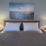 Doppelbett mit Kopfkissen, Nachttische und Wandbild mit Strandmotiv.