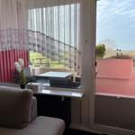 Durch das Fenster ist eine Terrasse mit Tisch und Stühlen zu sehen. Vor dem Fenster steht ein Sofa.