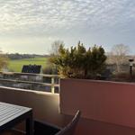 Terrasse mit Tisch und Stuhl. Blick auf grüne Wiesen und Häuser.