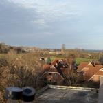 Blick auf Dächer, Bäume und Horizont mit Meer im Hintergrund.