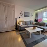 Wohnzimmer mit Sofa, Tisch und Kleiderschrank. Fenster mit Vorhängen.