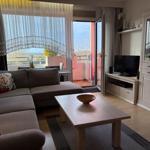 Wohnzimmer mit Sofa, Couchtisch und TV. Balkon mit Blick auf Landschaft.