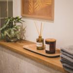 Holzregal mit Pflanze, Duftdiffusor und gefalteten Handtüchern.