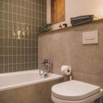 Bad mit Badewanne, Toilette und Holzregal mit Handtüchern.