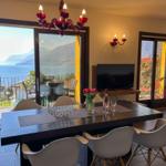 Dining room with lake and mountain view. Table, chairs, TV, and red ceiling lights.
