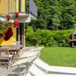 Garden with lounge chairs, table, grill, and red roses in front of yellow house.