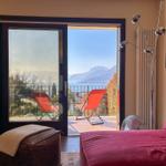Room with balcony, view of lake and mountains, red sun loungers, bed with pillows.