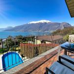 Terrasse mit Blick auf See und schneebedeckte Berge. Pool und Garten im Vordergrund.