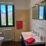 Badezimmer mit Fensterblick auf Berge, Waschbecken, Spiegel und rote Handtücher.