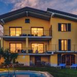 Ein gelbes Haus mit Balkonen und Pool im Garten bei Sonnenuntergang.