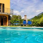 Pool mit Liegestühlen, Grill und gelbem Haus mit Balkon.