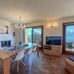 Wohn- und Essbereich mit Fernseher, Kamin und Blick auf See und Berge.