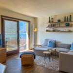 Wohnzimmer mit Sofa, TV und Balkonblick auf See und Berge.