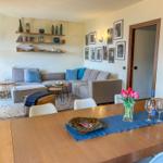 Ein Essbereich mit Tisch und Stühlen. Im Hintergrund ein Wohnbereich mit Sofa und Wandregalen.