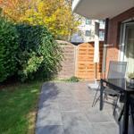 Terrasse mit Tisch, Stühlen und Sonnenschirm. Hinterhof mit Holztor und grüner Hecke.