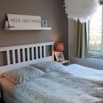 Schlafzimmer mit Bett, Nachttisch und Fenster. Wandregal mit Schriftzug.