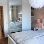 Schlafzimmer mit Spiegelschrank, Bett und Nachttisch. Durchgang zur Wohnfläche mit Sofa.