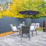 Terrasse mit Sitzgruppe, Sonnenschirm und Grillplatz. Hinterhof mit Grünfläche und Zaun.