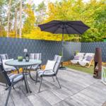 Terrasse mit Tisch, Stühlen, Sonnenschirm und Feuerstelle im Garten.
