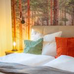 Schlafzimmer mit Bett, Kissen und Waldtapete an der Wand.