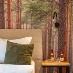 Schlafzimmer mit Waldtapete, Bett mit Kissen und Nachttisch mit Wein.