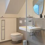Badezimmer mit Dusche, Waschbecken und Toilette unter Dachschrägen.