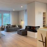 Wohnbereich mit Kamin, Sofa und Esstisch. Holzboden und große Fenster.