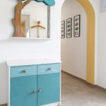 Ein Schrank mit blauen Schubladen und Türen unter einem Baumspiegel. Gelber Bogen im Hintergrund.