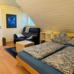 Schlafzimmer mit Bett, Sofa und Schreibtisch unter Dachschräge.