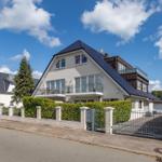 Modernes Haus mit Balkon und Gartenzaun unter blauem Himmel.