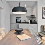 Dining area with table, chairs, and sofa. Kitchen with range hood and wall shelves.