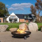 Fire pit in garden in front of house with large stones and trees.