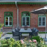 Red brick building with green window frames and garden furniture under a sun umbrella.