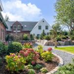 House with landscaped garden, stone path, and flower beds under blue sky.