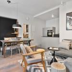 Living and dining area with sofa, table and chairs. Kitchen with refrigerator and oven.