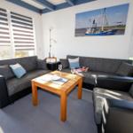 Wohnzimmer mit Sofa, Sessel und Tisch. Wandbild zeigt Fischerboot.