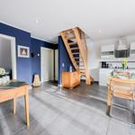 Küche mit Esstisch, Holztreppe und blauen Wänden. Wohnbereich mit Tisch und Blumen.