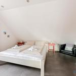 Schlafzimmer mit Doppelbett, Sessel und Spiegel an schräger Wand.