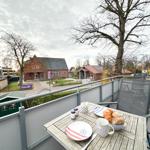 Terrasse mit Tisch, Stühlen und Frühstück. Blick auf Gebäude und Bäume.