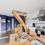 Küche mit Esstisch, Holztreppe und Schlafzimmer im Hintergrund.