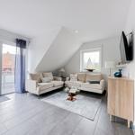 Wohnzimmer mit zwei Sofas, Glas-Tisch und TV. Balkon über Schiebetür. Dachgeschoss mit Dachschrägen.