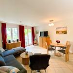 Wohnzimmer mit Sofa, Esstisch und TV. Rote Vorhänge, Holzmöbel und Fenster zur Terrasse.