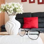 Auf dem Tisch liegt ein Buch mit Brille. Hinterher ein Sofa mit Kissen und Blumen.