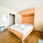 Schlafzimmer mit Bett, Küchenzeile und Sessel.