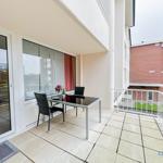 Terrasse mit Tisch und Stühlen, Blick auf Gebäude und Grünflächen.
