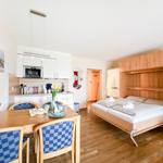 Schlafzimmer mit Bett, Küchenbereich und Esstisch mit Stühlen.