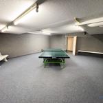 Raum mit Tischtennisplatte, Sitzbänken und Deckenleuchten.